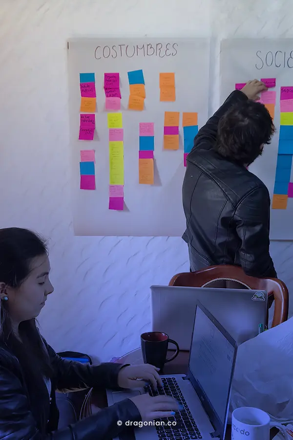 Equipo de trabajo exponiendo su lluvia de ideas en una cartelera, frente a compañeros que hacen fotos.